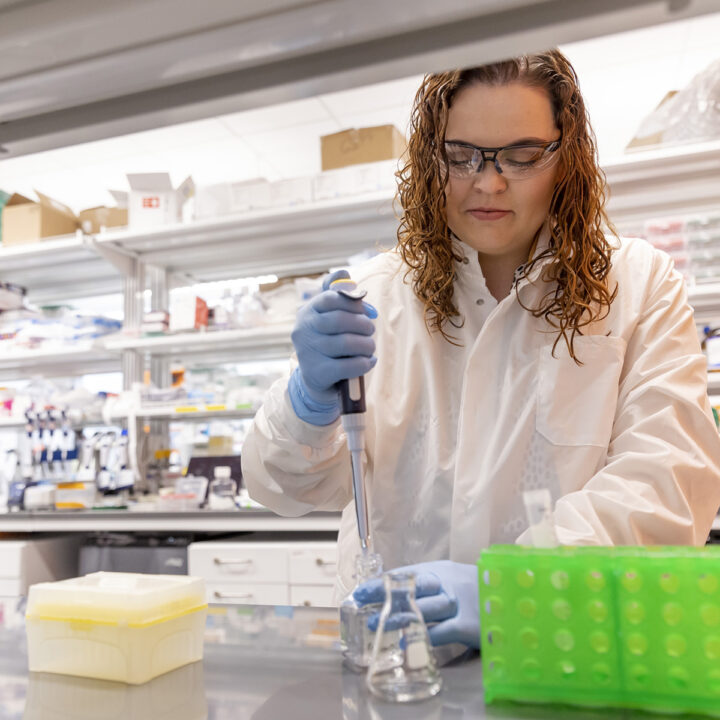 A scientist in a white coat pipettes into a conical flask