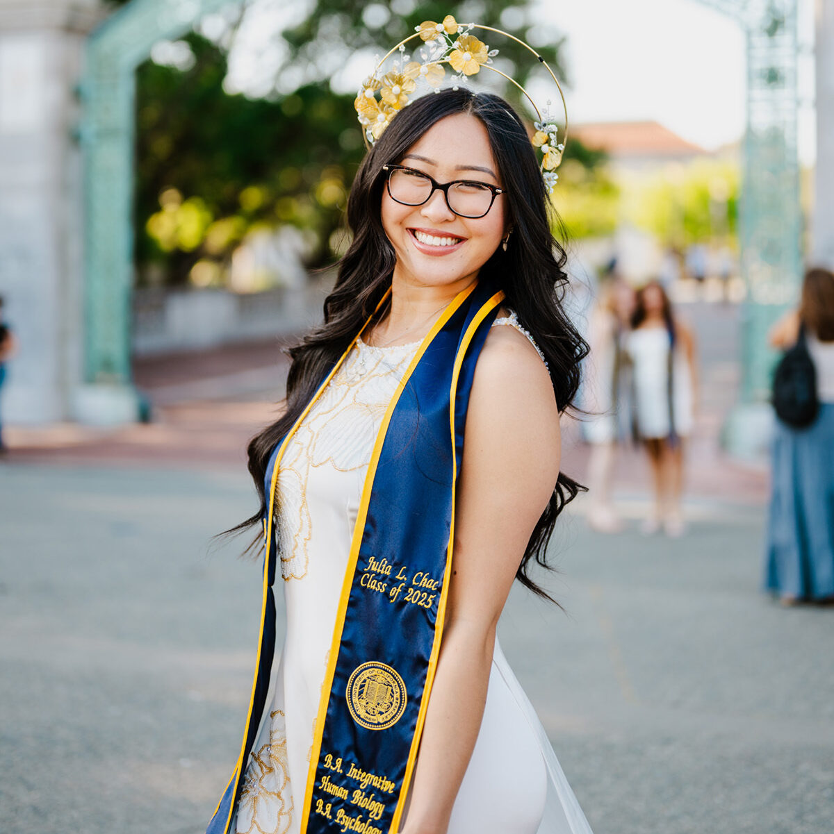 Julia posing at the UC Berkeley campus in a bright dress and her blue and yellow graduation sash.