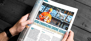 A person holds a magazine open to an article titled "How Embracing Drone Usage Can Transform Your Seaport Fortune," featuring a photo of a worker in safety gear holding a tablet with a drone flying nearby.