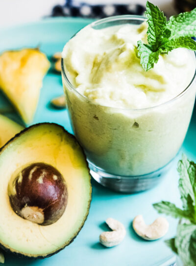 A cut avocado next to an avocado smoothie garnished with fresh mint