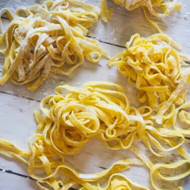 Piles of flour dusted paleo fettuccine on a white wooden board.