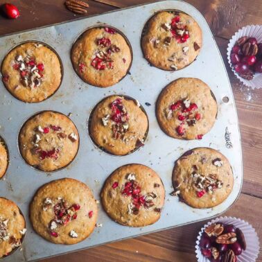 Freshly baked cranberry orange muffins sprinkled with pecans still in the muffin tin.