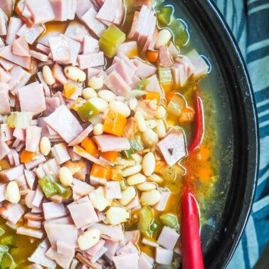 A crockpot filled with white beans and ham, cooking.