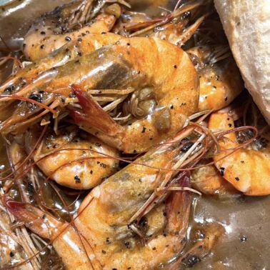 Cooked BBQ shrimp in a bowl with a loaf of crunchy bread.