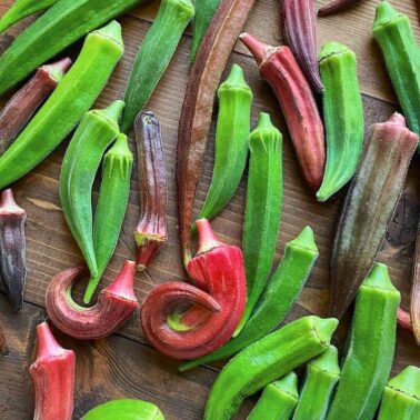 A spread of fresh okra pods in varying shades of green and purple on a wooden surface.