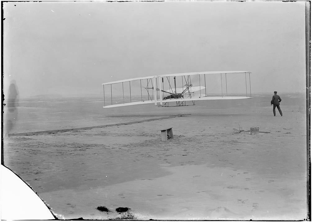 Wright Flyer, on its first flight, Kill Devil Hills, North Carolina, 17 December 1903. Orville Wright is on board and Wilbur Wright is just to the right of the airplane. (John T. Daniels/Library of Congress Prints and Photographs Division LC-DIG-ppprs-00626)