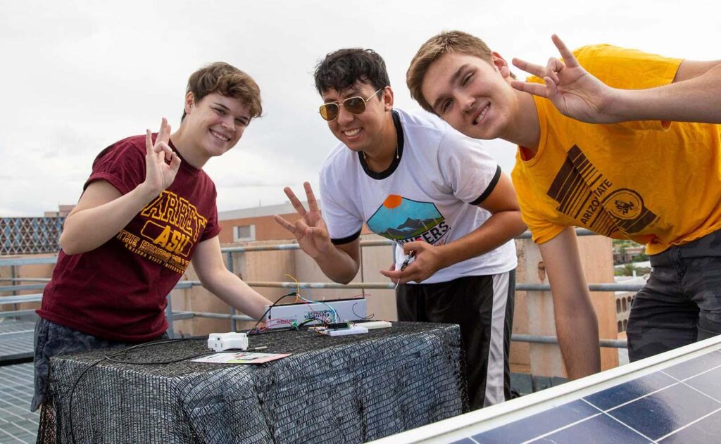 Three students working on their project for the Summer Research Internships (SURI) program, smiling and making the pitchfork hand sign.