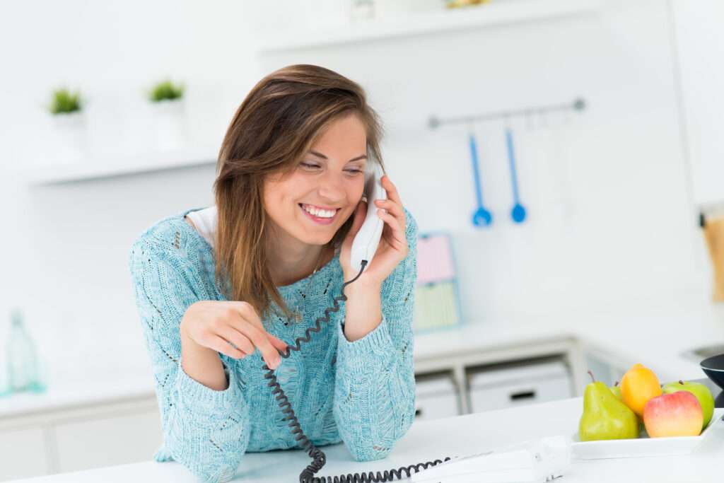 Woman talking on corded residential phone line smiling