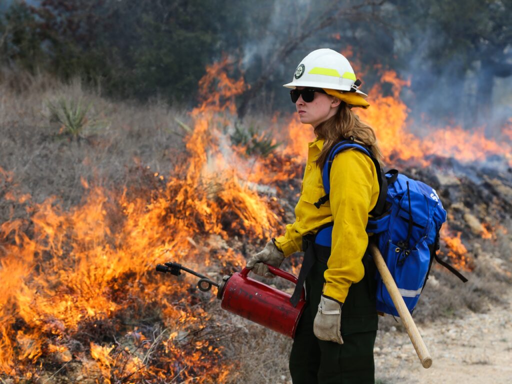 Female firefighter holding a drip tourch in front of fire