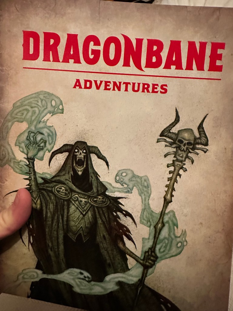 The cover of Dragonbane Adventure book from the boxed set. A lich stands with a greenish energy coming from one hand and the other holds a skull-topped staff.