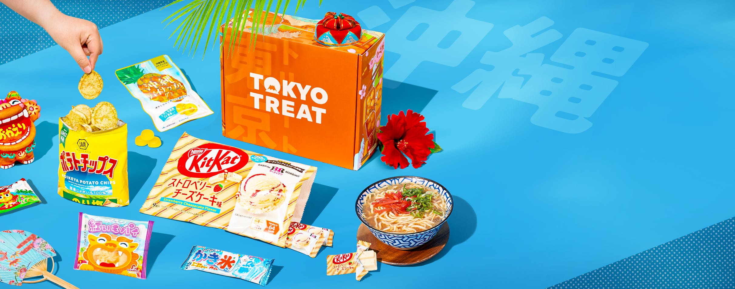 Orange TokyoTreat box on blue background with Okinawa-themed snacks around it