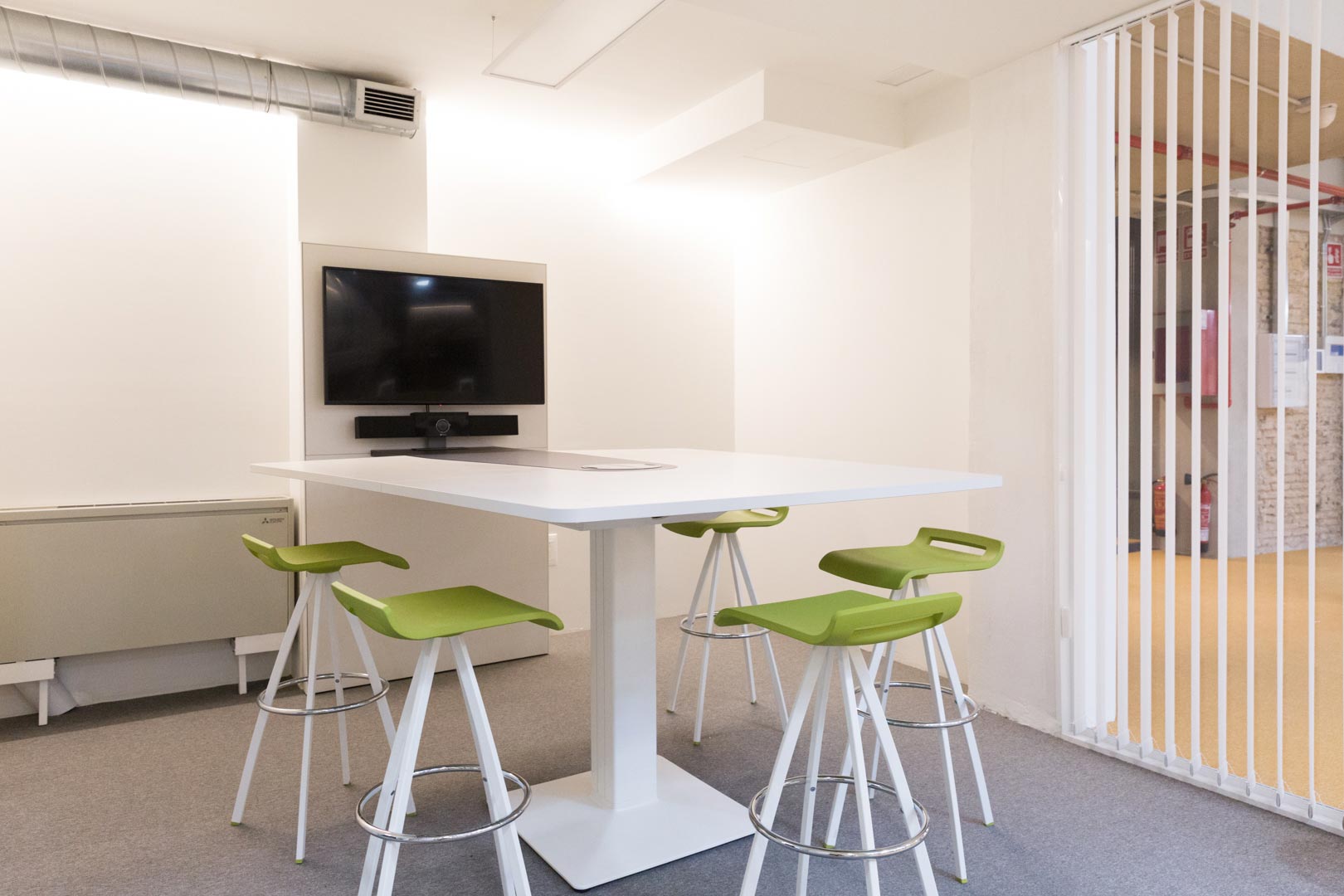 Mesa de reuniones con sillas y televisor en sala de oficina.