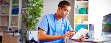 Man in scrubs with stethoscope looking at a tablet
