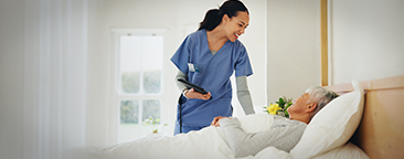 Woman in scrubs taking care of elderly woman in a bed