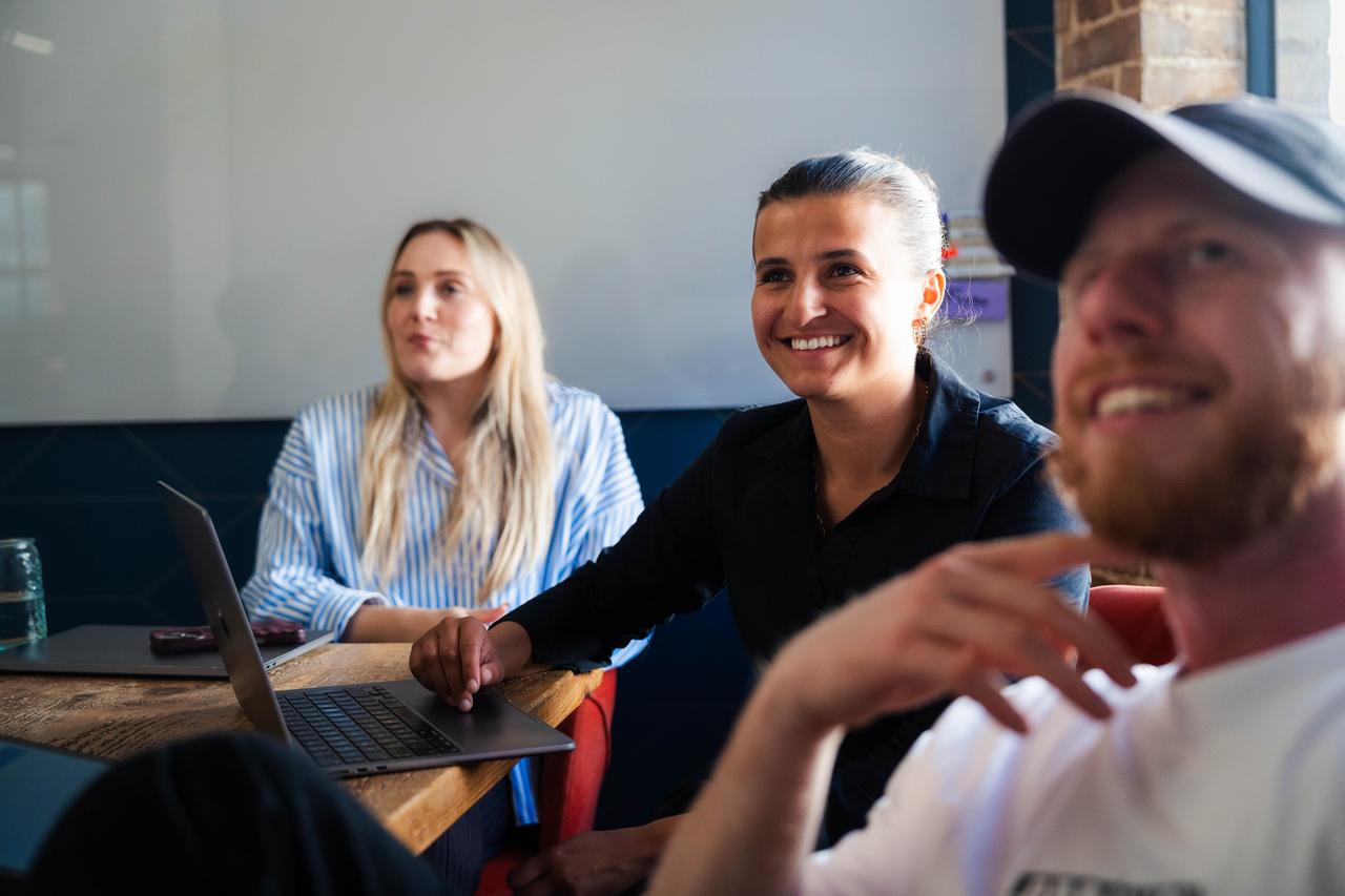 Three people — two white women and a white man — sit at a table viewing a laptop. Taken during a social media advocacy training session supporting employee-generated content.