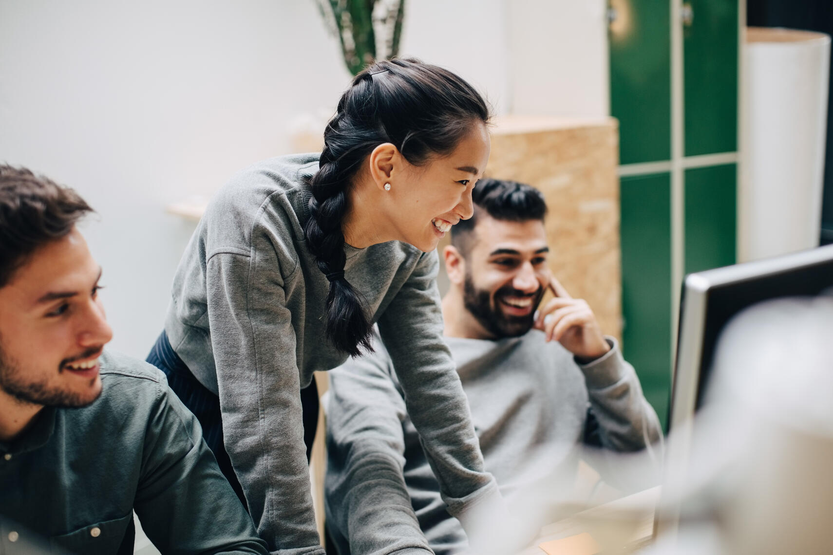 Woman standing over desk with computer, smiling with coworkers.