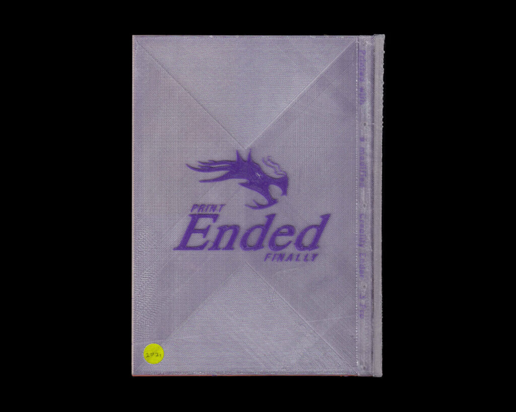 A 3D printed book-inspired object with a purple dragon graphic, the words “PRINT Ended” and “FINALLY!” on its surface, plus a small yellow circle in the lower left corner marked “2/3.”.