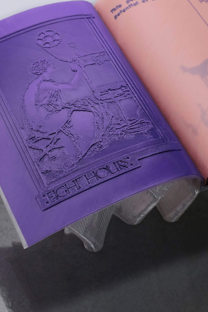 A purple embossed page in a 3D printed book shows a classical-style figure beside a loom with the text EIGHT HOURS underneath; part of a peach-colored page is visible on the right.