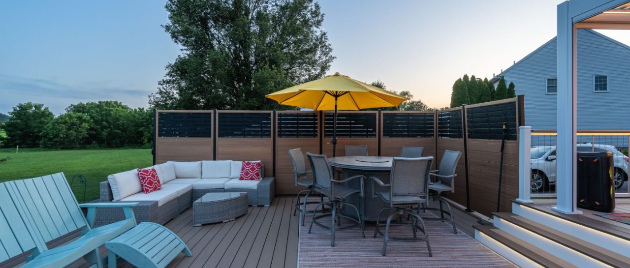 composite backyard deck with privacy screen, outdoor furniture, and yellow umbrella at sunset