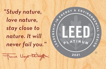 Wooden background with a quote about nature by Frank Lloyd Wright in red text. Beside it, a circular LEED Platinum certification badge from 2021.