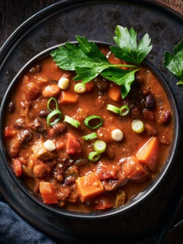 Top down shot of chili in bowl on plate on wood surface.