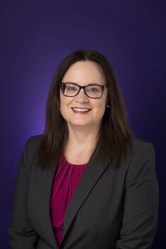 Woman wearing a black blazer smiling with glasses.
