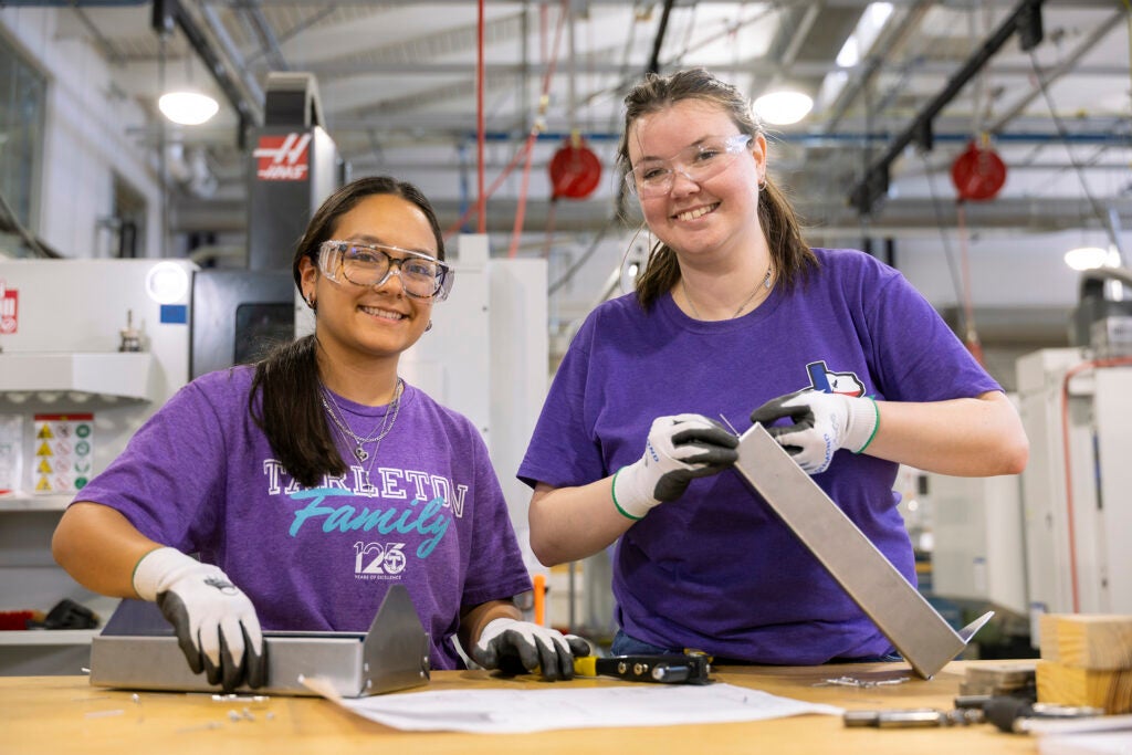 Two girls wearing purple shirts with metal in there hands.