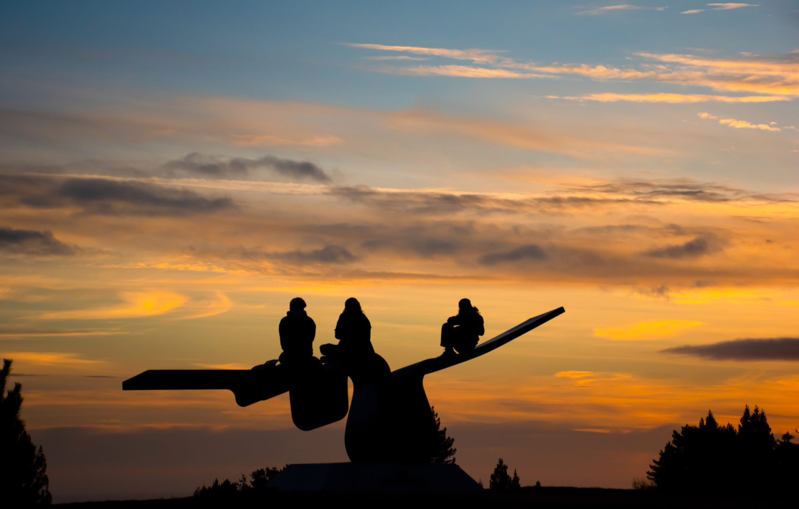 Three students sit on the "Porter Squiggle" sculpture and watch the sunset