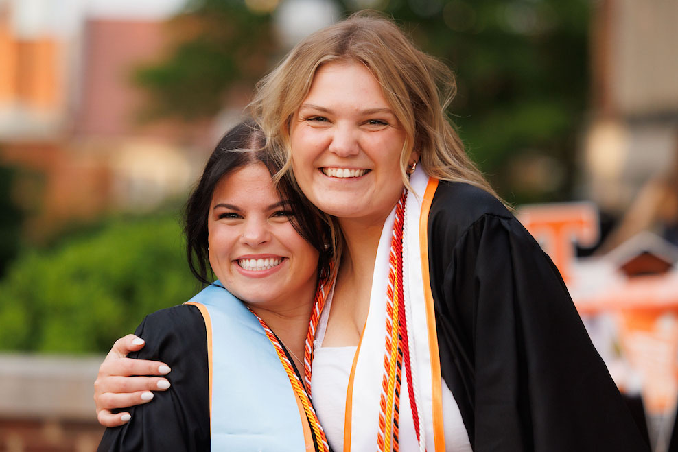 Two graduates smile and pose together in academic regalia during Torch Night: A Farewell to Thee on Ayres Lawn. Photo by Steven Bridges, University of Tennessee