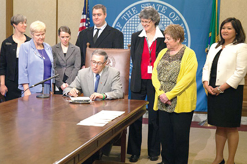 People standing around a man signing a document on a table